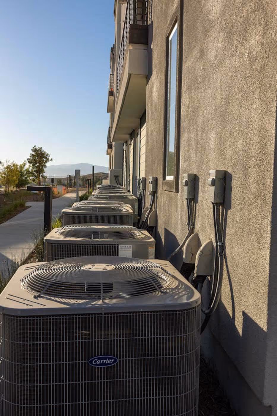 Row of outdoor Carrier air conditioning units installed along the side of a building under a clear sky.